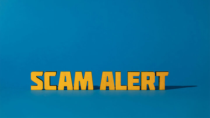 Color-colored text on a blue surface, spelling Scam Alert.