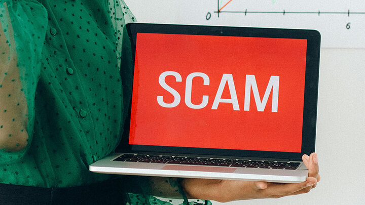 Woman in a green blouse holding a laptop with a red screen and the word Scam.